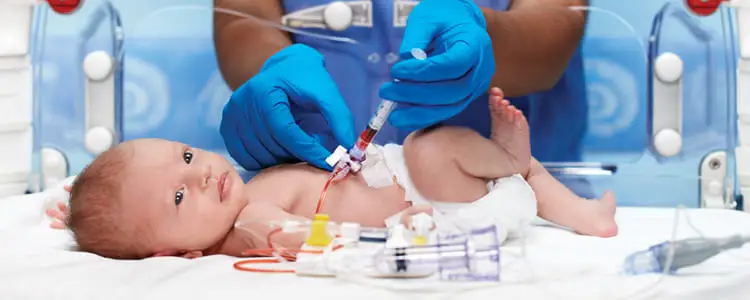 Neonatal intensive care procedure with a newborn baby lying in an incubator while a clinician in blue gloves injects medicine through a catheter, representing specialised pediatric urologist treatment in Indore by Dr. Pritesh Shrimali, best urologist in Indore.
